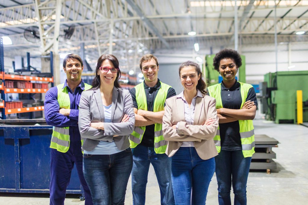 Group portrait of staff at distribution warehouse. Warehouse team standing with arms crossed in factory.